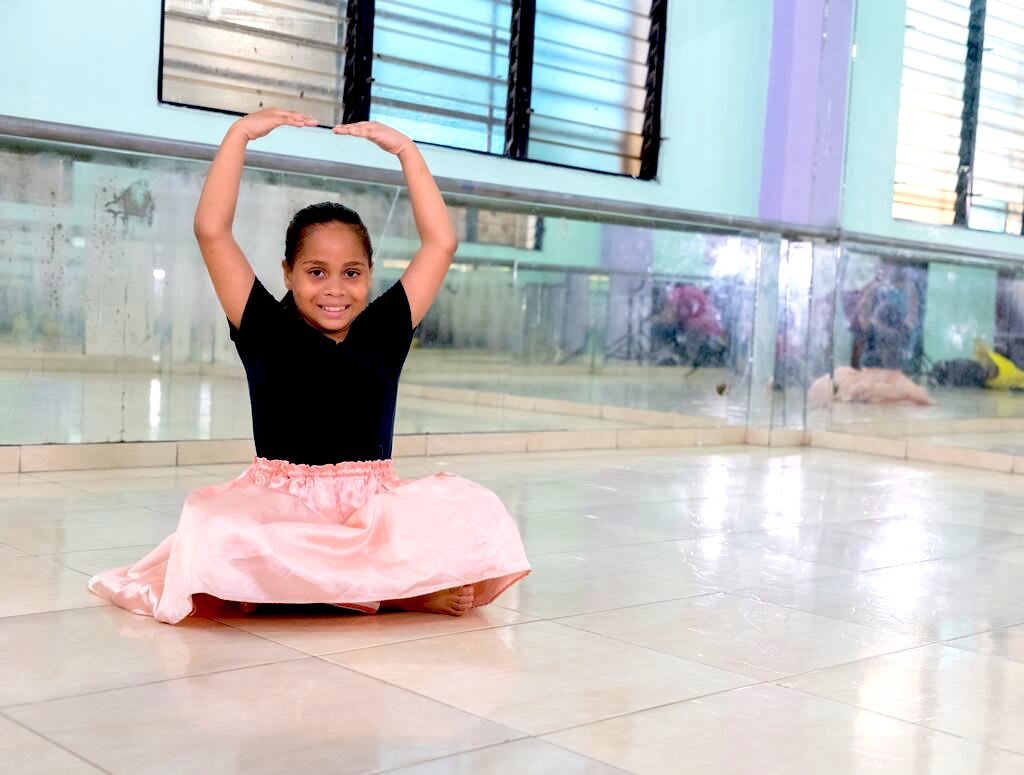Aime sits on the ground wearing her tutu